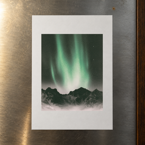 Unframed A4 northern lights print from Igor Grushko lying flat on a brushed stainless steel surface.